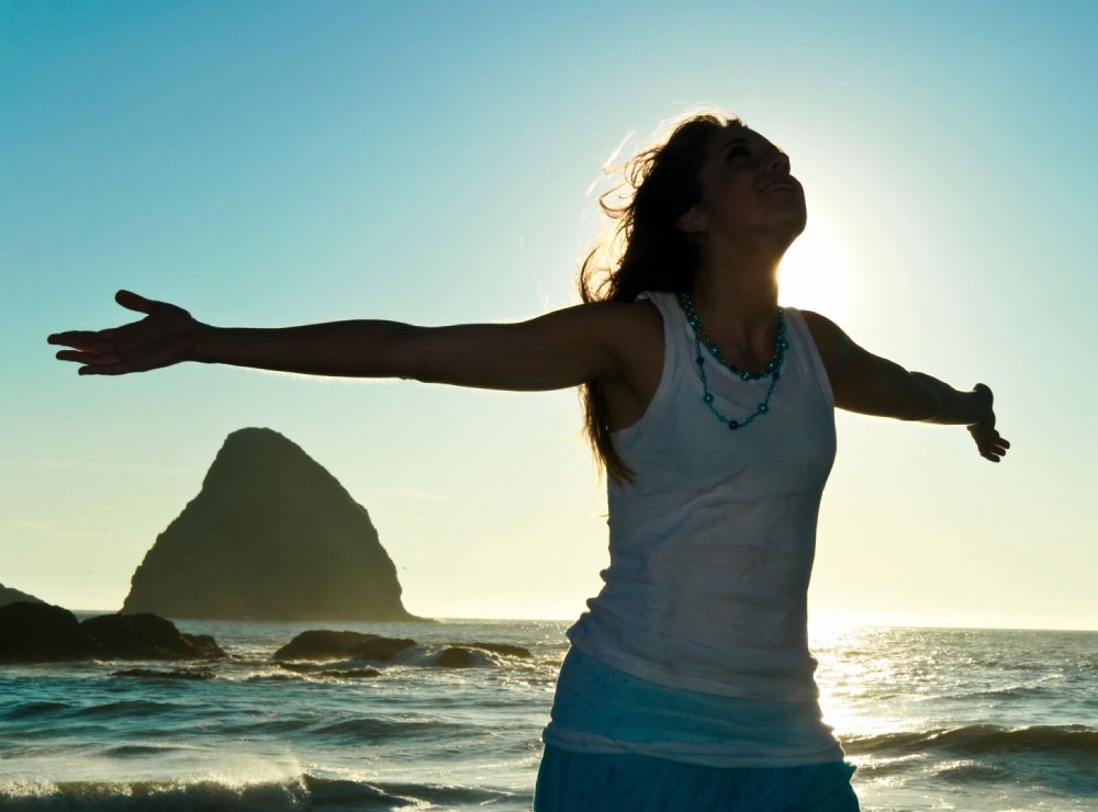 Joanna Blu, naturopathe, thérapeute et guide, au bord de mer, les bras ouverts regardant le ciel